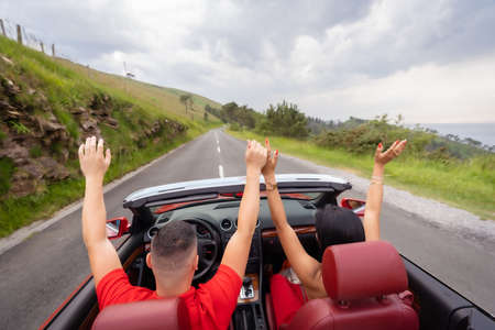 A couple in a convertible car enjoying the summer with their arms up in a sunsetの写真素材