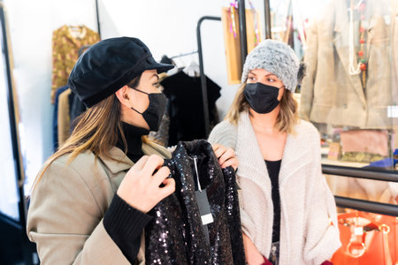 Caucasian employee of a luxury clothing store showing a sequin dress in front of a mirror, security...