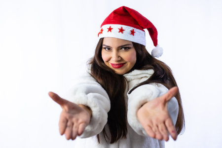 Pretty latin girl in xmas with a white background, wearing a christmas hat with stars, with open arms celebrating christmas in winterの写真素材