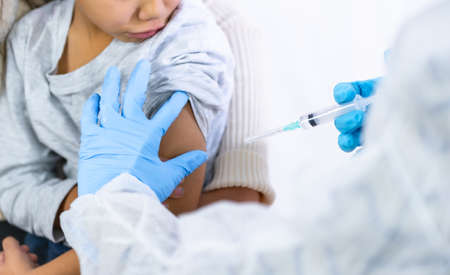 A female doctor injecting the vaccine to a child with his mother. Vaccination of children for immunization in the coronavirus pandemic, covid-19の写真素材