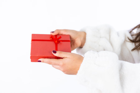 Hands of a young Latin brunette girl joyfully handing over a gift on a white background. I challenge the model with a red gift boxの写真素材