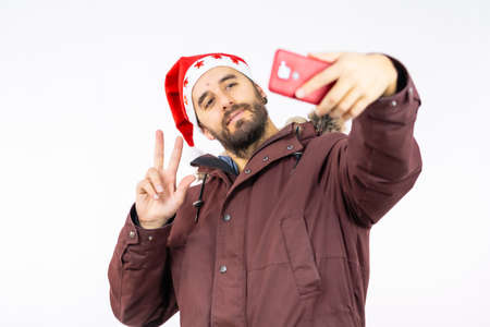 Very happy young caucasian man with the red christmas hat taking a selfie on a white backgroundの写真素材