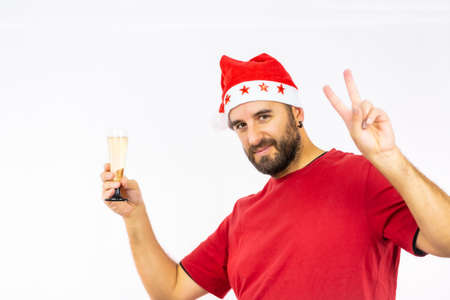 Young very happy Caucasian man with red Christmas hat toasting with a glass of champagne on a white background, dressed in a red shirtの写真素材