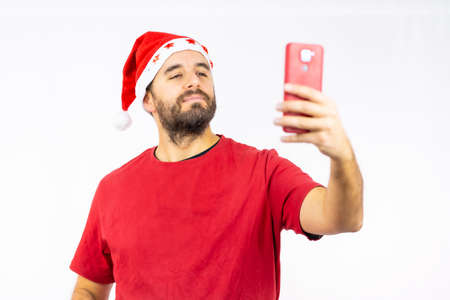 Young man with the red christmas hat taking a selfie on a white background, dressed in a red t-shirt, copy pasteの写真素材