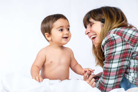 Baby boy in a studio with a white background, eight month old Caucasian newborn sitting and playing with his motherの写真素材