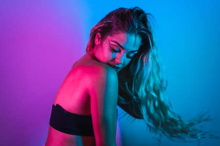 A Caucasian blonde girl with eye drawing makeup, eyelashes arranged on a blue background with pink neon lightsの写真素材