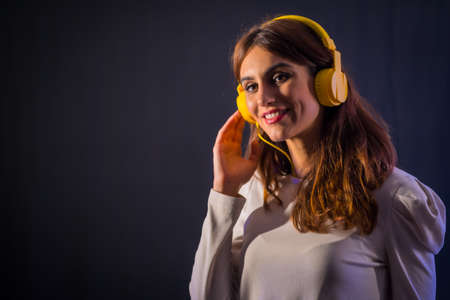 Young caucasian brunette with yellow headphones on a black background, smiling looking in a nightclubの写真素材