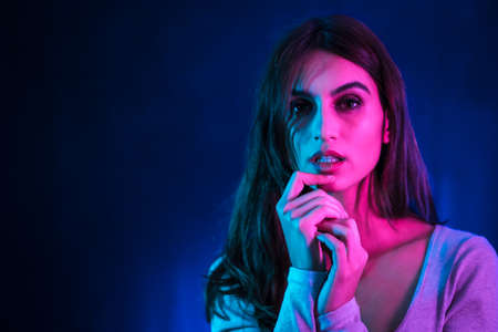 A young brunette Caucasian woman in a white t-shirt dancing in a nightclub with a black background. Neon lights, portrait looking at cameraの写真素材