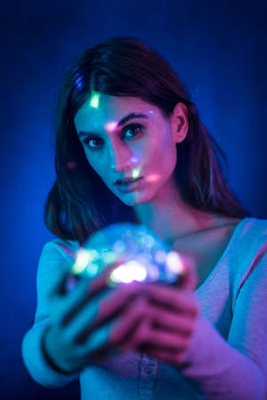 A young brunette Caucasian woman in a white t-shirt on a black background. Neon lights, illuminated with a disco light in hand, vertical photoの写真素材