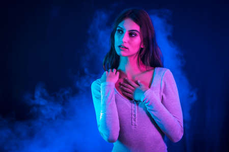 A young brunette Caucasian woman in a white t-shirt in a nightclub with a black background. Neon lights, portrait with sweet lookの写真素材
