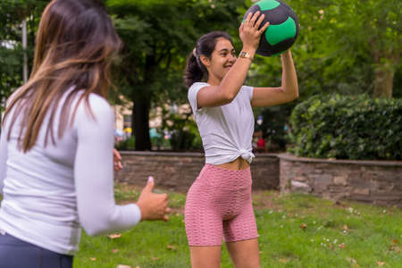 Latin girl doing sports in a green park, lifestyle a healthy life, attentive teacher with the students in the exercise of squats with the weight ballの写真素材