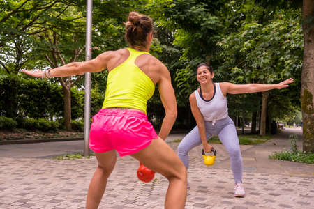 Latin girl doing sports in a park in the city, lifestyle a healthy life, two girls doing stretching weights and squatsの写真素材