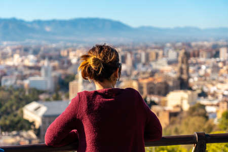 A young woman looking at the views of the city and the Cathedral of the Incarnation of Malaga from the Castillo de Gibralfaro in the city of Malaga, Andalusia. Spainの写真素材