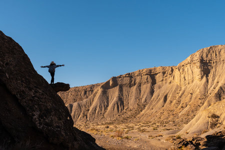 Silhouette of a free young woman with open arms climbing a rock in the desert of Tabernas, province...