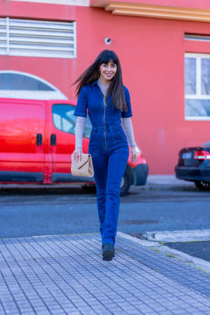 Posing of a brunette model walking down the street with a denim suit. Caucasian pretty a background of red housesの写真素材