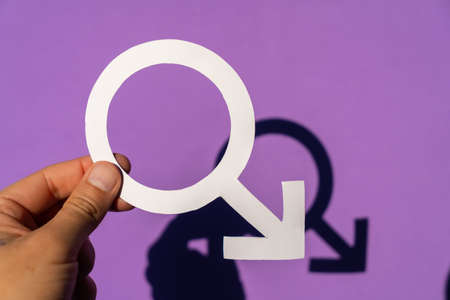 A man holding the male symbol on a purple background and his beautiful shadow is seen, also fighting for women's rights and equalityの写真素材