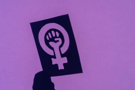 Shadow of the symbol of the fight for feminism on a purple background, clenched fist of a woman in the march protests for women's rightsの写真素材