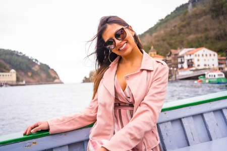 Pretty latin woman smiling with sunglasses sightseeing on a boat along the coast. Tourism in summer on vacation, Pasajes San Juan, near San Sebastian. Gipuzkoa, Basque Countryの写真素材