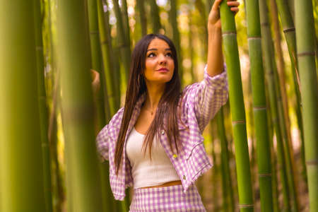 Young caucasian girl with a pink skirt in a bamboo forest. Enjoying summer holidays in a tropical climate, lifestyle of a girl walking and smiling in the forestの写真素材