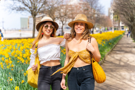 Friends in the city with straw hats walking and smiling next to some beautiful yellow flowers,...