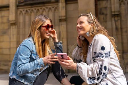 Listening to music in the city, two caucasian friends sharing the headphones and listening to the latest musicの写真素材