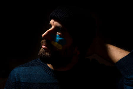Stop war, conflict between Ukraine and Russia. A young Ukrainian with his face painted in the colors of the blue and yellow flag. black backgroundの写真素材