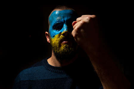 Stop war, conflict between Ukraine and Russia. Portrait of a young man with his face painted in the blue and yellow colors of the flag. Wanting to fight for his countryの写真素材