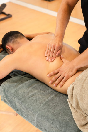 An athletic man receiving a recovery massage by a physiotherapist on a stretcher, detail of the...