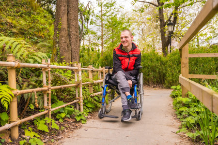 Portrait of a paralyzed young man in a public park in the city. Sitting in the wheelchair strolling...
