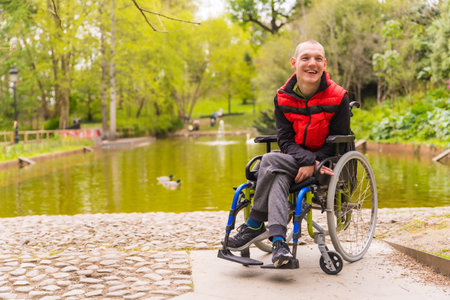 A paralyzed young man in a public park in the city. Sitting in the wheelchair