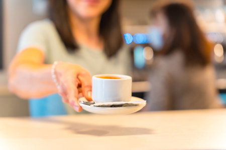 Hands of female coffee shop owner with a latte in her hand, offering the coffee to the customerの写真素材