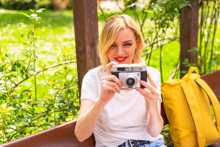 A tourist girl enjoying the photos she has taken on vacation in a park in the city, wearing a hat...