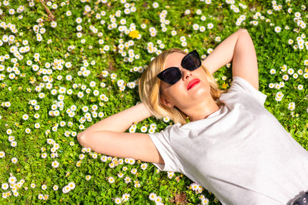A young blonde girl in a hat and sunglasses breathing pure hair in the spring in a park in the city,...