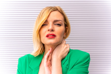 Portrait of a beautiful blonde model in a green jacket on a gray background in the city, in a fashion poseの写真素材