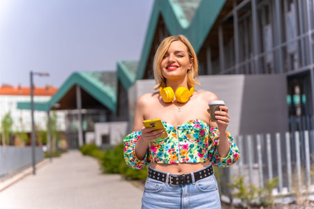 Portrait of a blonde woman walking with the phone through the city with yellow headphones and a take...