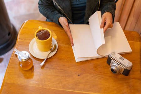 A tourist girl with a photo camera drinking tea on a cafeteria terrace. Reading a bookの写真素材
