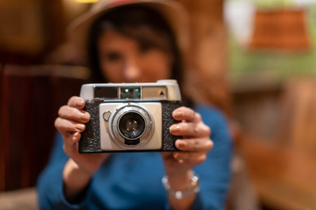 A pretty tourist with a hat and a photo camera drinking tea in a cafe, taking some photos with the...