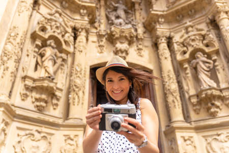 Tourist woman smiling with hat visiting the city and taking photos with a camera, enjoying summer vacation, concept of female traveler and digital content creatorの写真素材