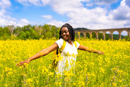 Enjoying freedom, a black ethnic girl with braids, a traveler, in a field of yellow flowers
