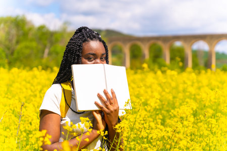 Reading a book in nature, a girl of black ethnicity with braids, a traveler, in a field of yellow...