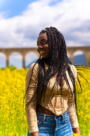 Lifestyle moving hair, portrait of black ethnic girl with braids, traveler, in a field of yellow...
