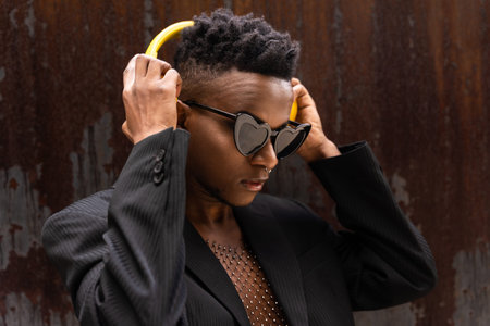 Black ethnic man listening to music wireless yellow headphones, wearing heart sunglasses, listening...