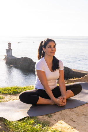 A woman doing yoga exercises in nature by the sea, ardha padmasana