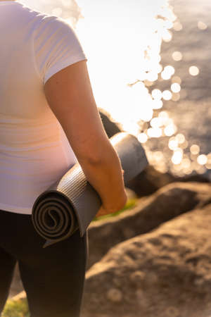 Hands of a woman with the yoga mat in nature by the sea at sunset, healthy and naturist life, pilates outdoorsの写真素材