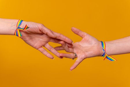 Detail of two hands of two women caressing and touching each other's fingers, LGBT concept on a yellow background, couple of lesbian girlsの写真素材