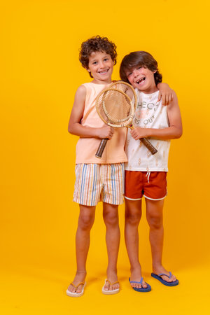 Portrait of two brothers playing tennis on summer vacation, yellow backgroundの写真素材