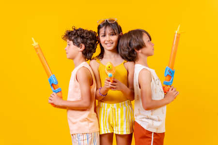 Brothers having fun with water pistols on summer vacations and aiming at camera, yellow backgroundの写真素材
