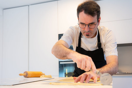 Man cooking homemade croissants, measuring puff pastry and making cuts, work at home