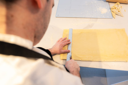 Man cooking homemade croissants, measuring puff pastry and making cuts, work at home