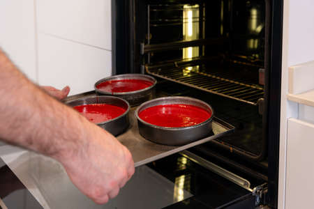 Hands of a man cooking a red velvet cake at home, putting the red cake in the oven, work at homeの写真素材